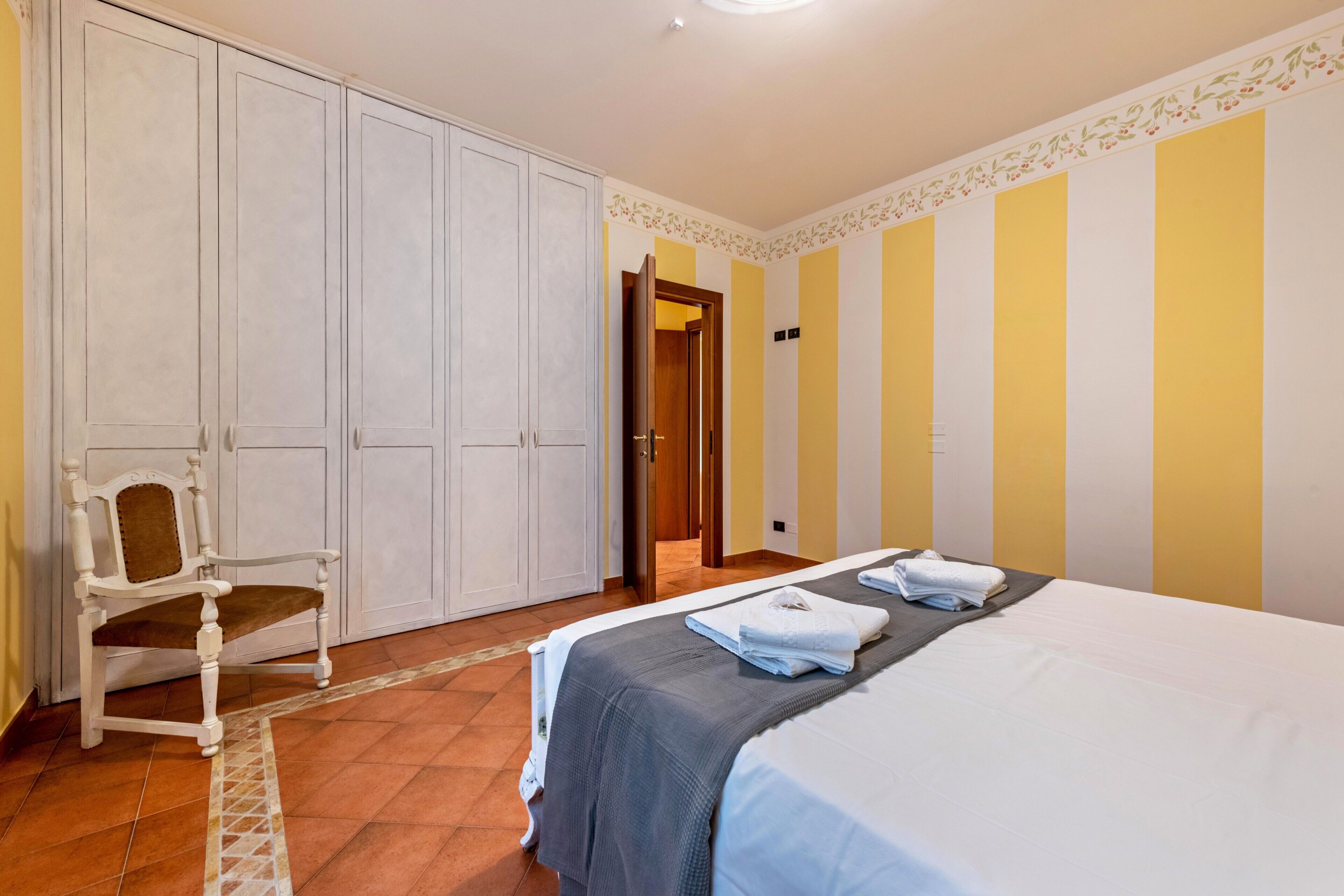 Une chambre à coucher comprenant un lit, une armoire, une chaise et une porte donnant sur une autre pièce.