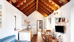 A compact kitchen with a sink, stove, and white tiles. There is a dining area with a table and chairs, a sofa, and a TV mounted on the wall. - Casa Silla Vieja Uno, private terrace and balcony in Vejer de la Frontera (Vejer de la Frontera)