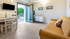 Un salon comprenant un canapé, une table à manger avec des chaises, un téléviseur fixé au mur et une porte-fenêtre coulissante donnant sur un espace extérieur.
