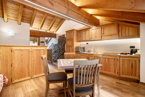 A wooden interior with a dining table and chairs, a kitchen area with wooden cabinets, and a stone wall.