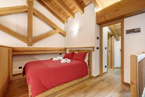 A bedroom with a wooden ceiling, a bed with red bedding, and a wooden floor.