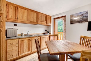 Una cocina de madera con una mesa de comedor y sillas, un tostador y una ventana con vistas a la vegetación.