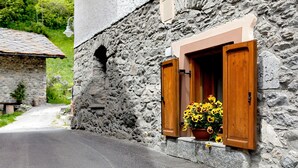 Un bâtiment en pierre doté d’une fenêtre ornée de volets en bois et d’un pot de fleurs contenant des fleurs jaunes.