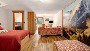 Une chambre d’hôtel avec deux lits, un plancher en bois, un coin repas et un grand tableau représentant un paysage de montagne.