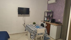 Une petite pièce, de taille modeste, comprenant une table à manger, une seule chaise, un téléviseur fixé au mur, un lave-linge et un coin cuisine.