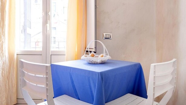 Une pièce avec une table recouverte d’une nappe bleue, une chaise blanche et un panier contenant du pain, posé sur la table.