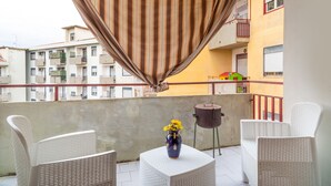 Een balkon met rieten stoelen, een kleine tafel met een vaas, en een barbecue.