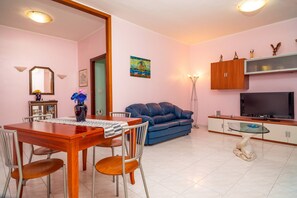 Ein Wohnzimmer mit Esstisch, Stühlen, einer Couch, einem Fernseher und einem Schrank.