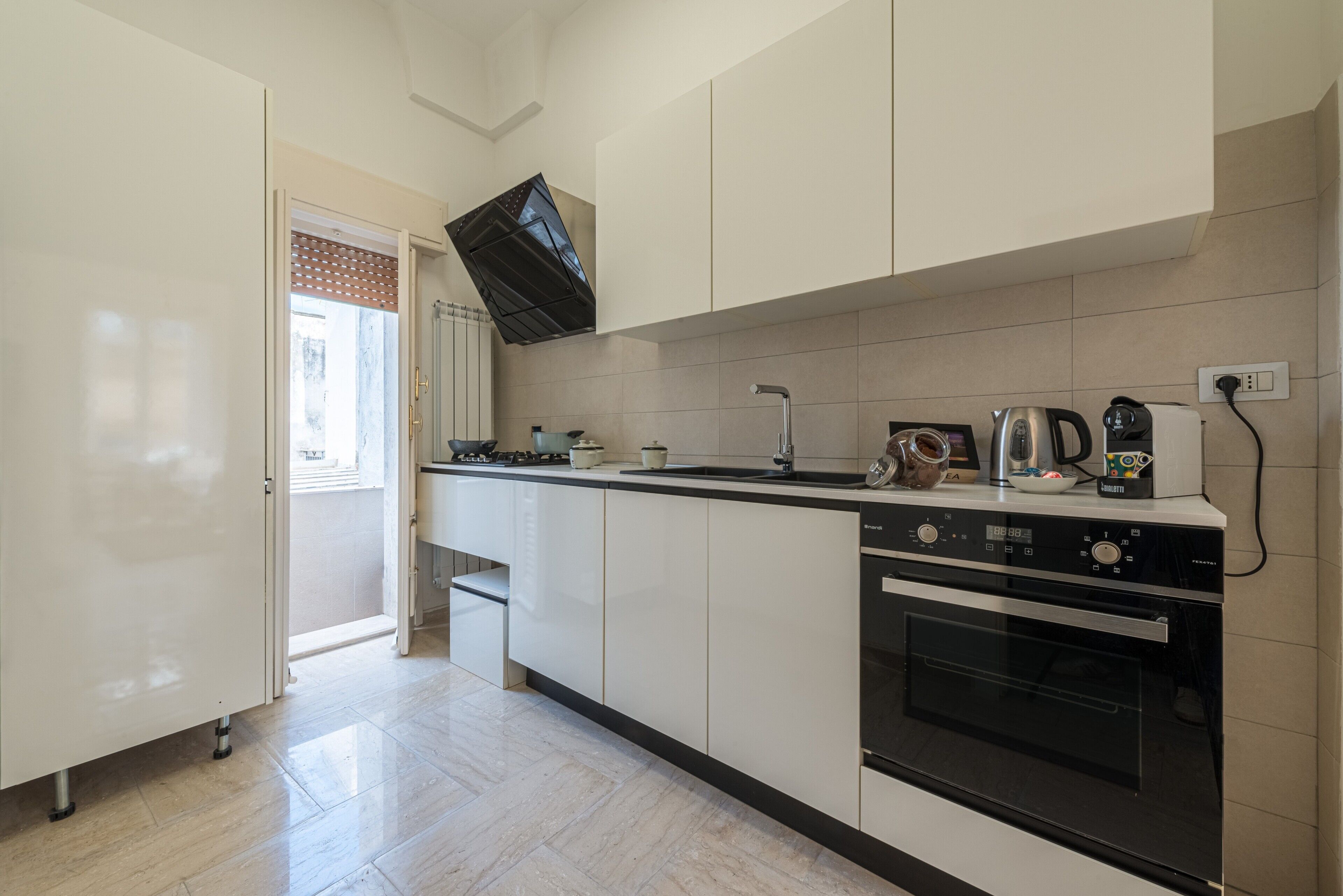 Una cocina moderna con armarios blancos, horno empotrado, estufa y hervidor.
