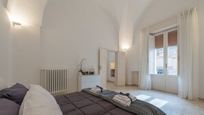 Ett sovrum med en stor säng, ett element, en byrå, en spegel och ett fönster med gardiner.