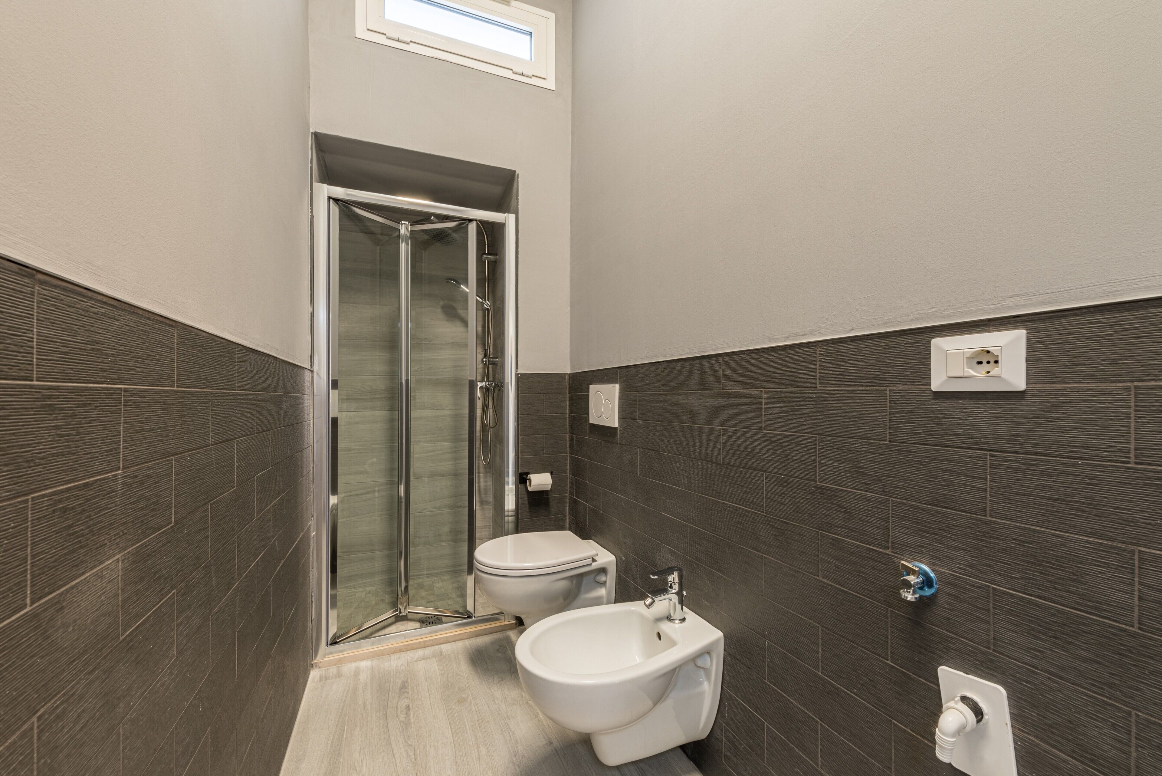 A bathroom with a shower, toilet, and bidet, tiled walls, and a window.
