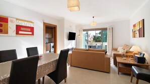 A modern living room with a dining area, a sofa set, a TV, and a kitchen in the background. - Apartment 'Condomínio Quinta Do Vale' with Shared Pool, Wi-Fi and Air Conditioning (Guia)