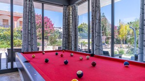 A pool table with balls, large windows, and a view of outdoor plants and buildings. - Villa 'Joel' with Sea View, Wi-Fi and Air Conditioning (Fontane Bianche)