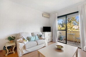En stue med sofa, fjernsyn, bord og en balkon med stole.