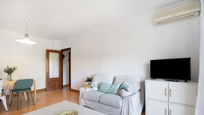 A living room with a sofa, TV stand, and dining area. - Apartment 'Casa Pepe' with Private Terrace, Shared Garden and Wi-Fi (Jerez de la Frontera)