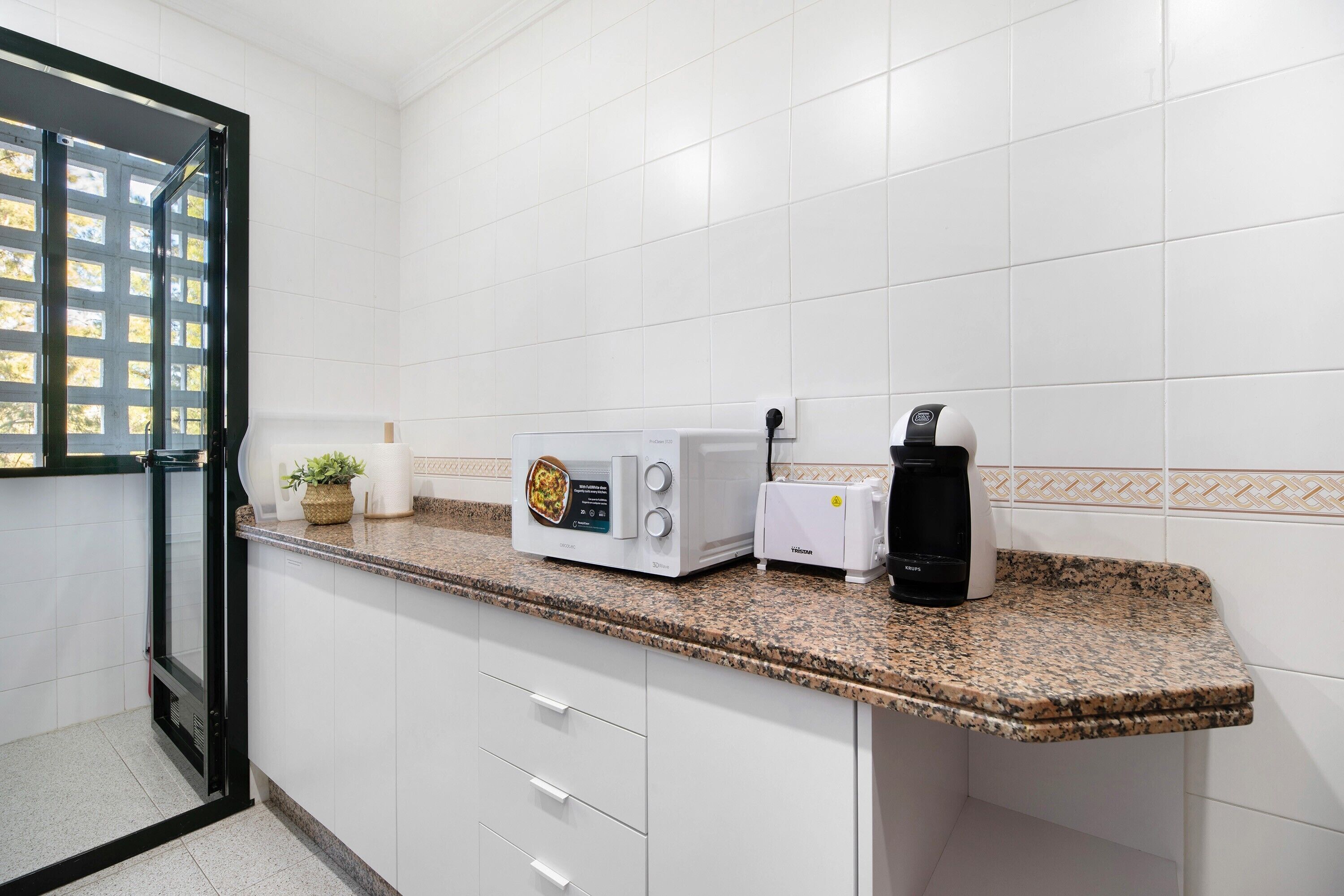 Eine Küche mit weißen Schränken, einer Granit-Arbeitsplatte, einer Mikrowelle, einem Toaster und einer Kaffeemaschine.