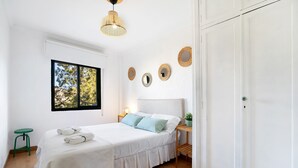 A bedroom with a bed, bedside table, lamp, and a window with a view of trees. - Apartment 'Casa Pepe' with Private Terrace, Shared Garden and Wi-Fi (Jerez de la Frontera)