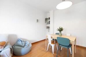 Une pièce comprenant une table à manger en bois, deux chaises, un fauteuil poire, un canapé blanc et un luminaire suspendu.