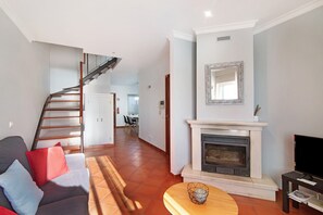 Un salon avec un canapé, une cheminée, un téléviseur et un escalier.