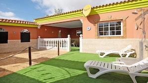 Un edificio con techo amarillo, antena parabólica y patio con césped artificial y sillones de descanso.