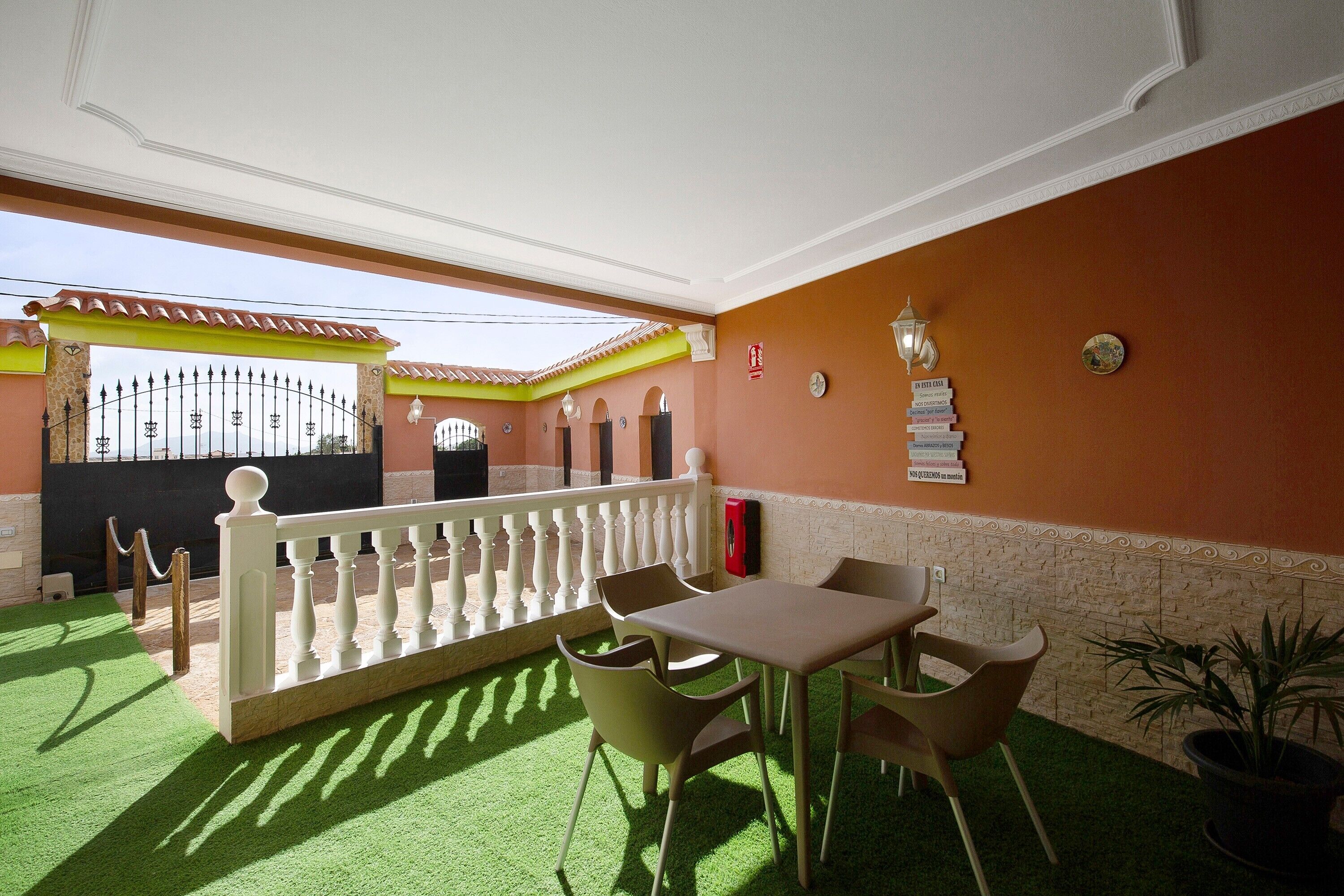 Una habitación con balcón, una mesa con sillas, una planta en maceta y un detalle decorativo en la pared.