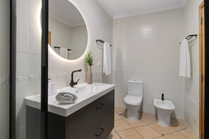 Une salle de bain moderne avec un meuble-lavabo blanc, un miroir rond, des toilettes et un bidet.