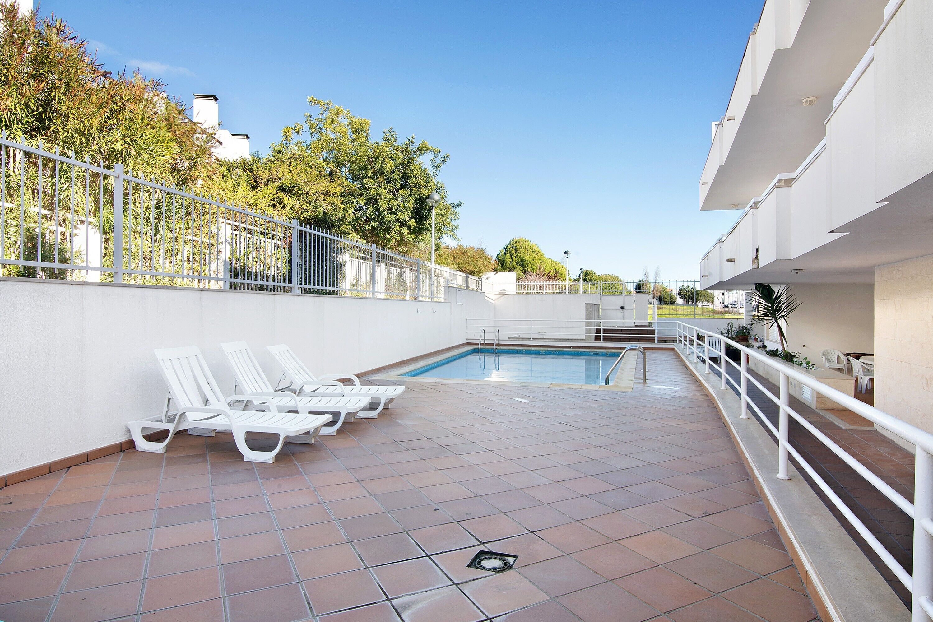 Un espace piscine avec des chaises longues blanches, un sol carrelé et une rambarde blanche.