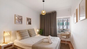 Une chambre bien rangée, avec un lit, des lampes de chevet, une chaise et une fenêtre avec des rideaux.