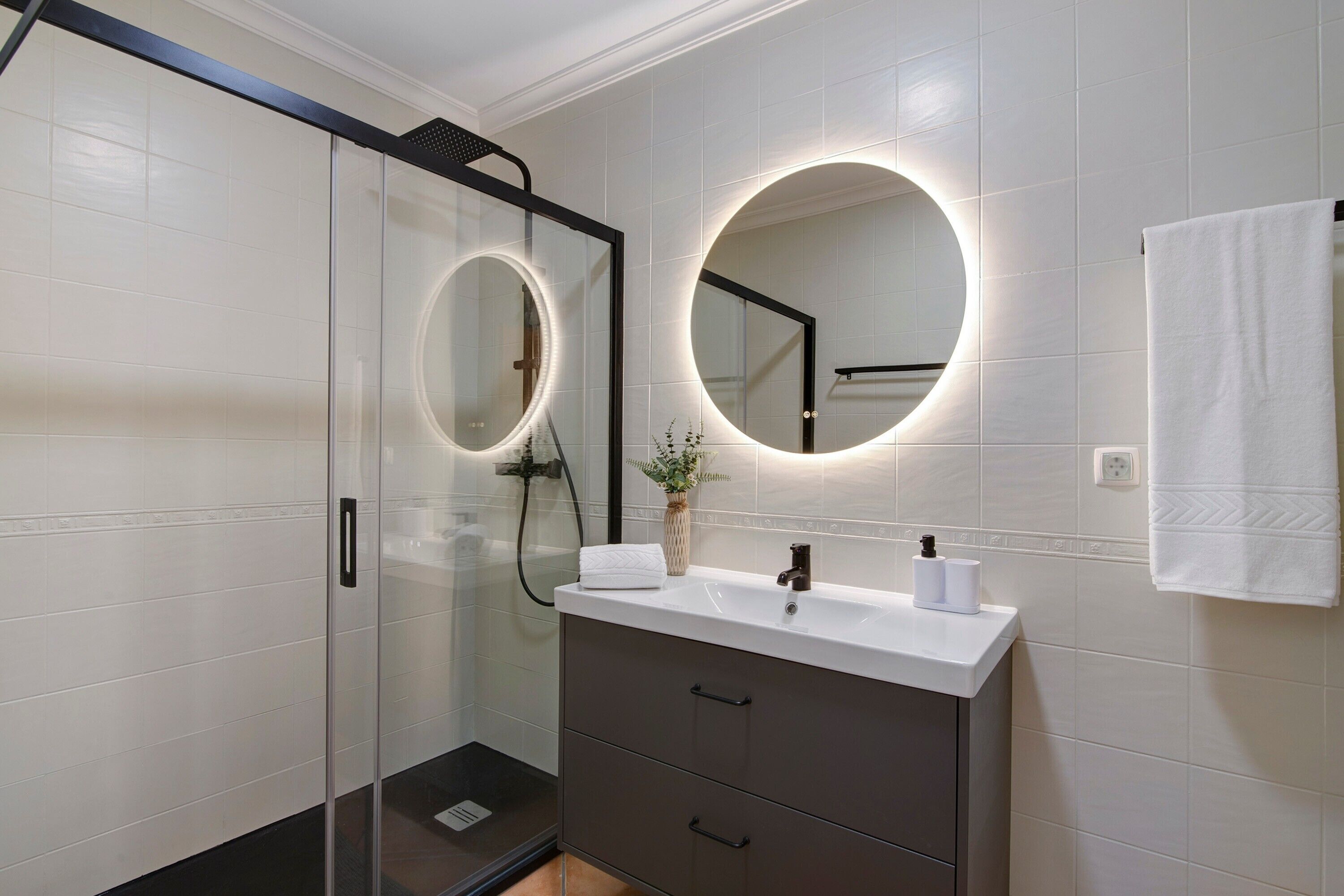 A modern bathroom with a glass shower enclosure, a vanity with a mirror, and a towel rack.