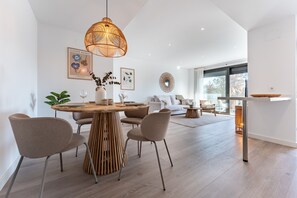 A modern dining area with a round wooden table, four chairs, and a hanging light fixture.