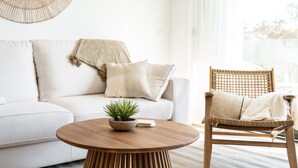 A modern living room with a white sofa, a wooden chair, a round wooden coffee table, and a woven wall decoration.