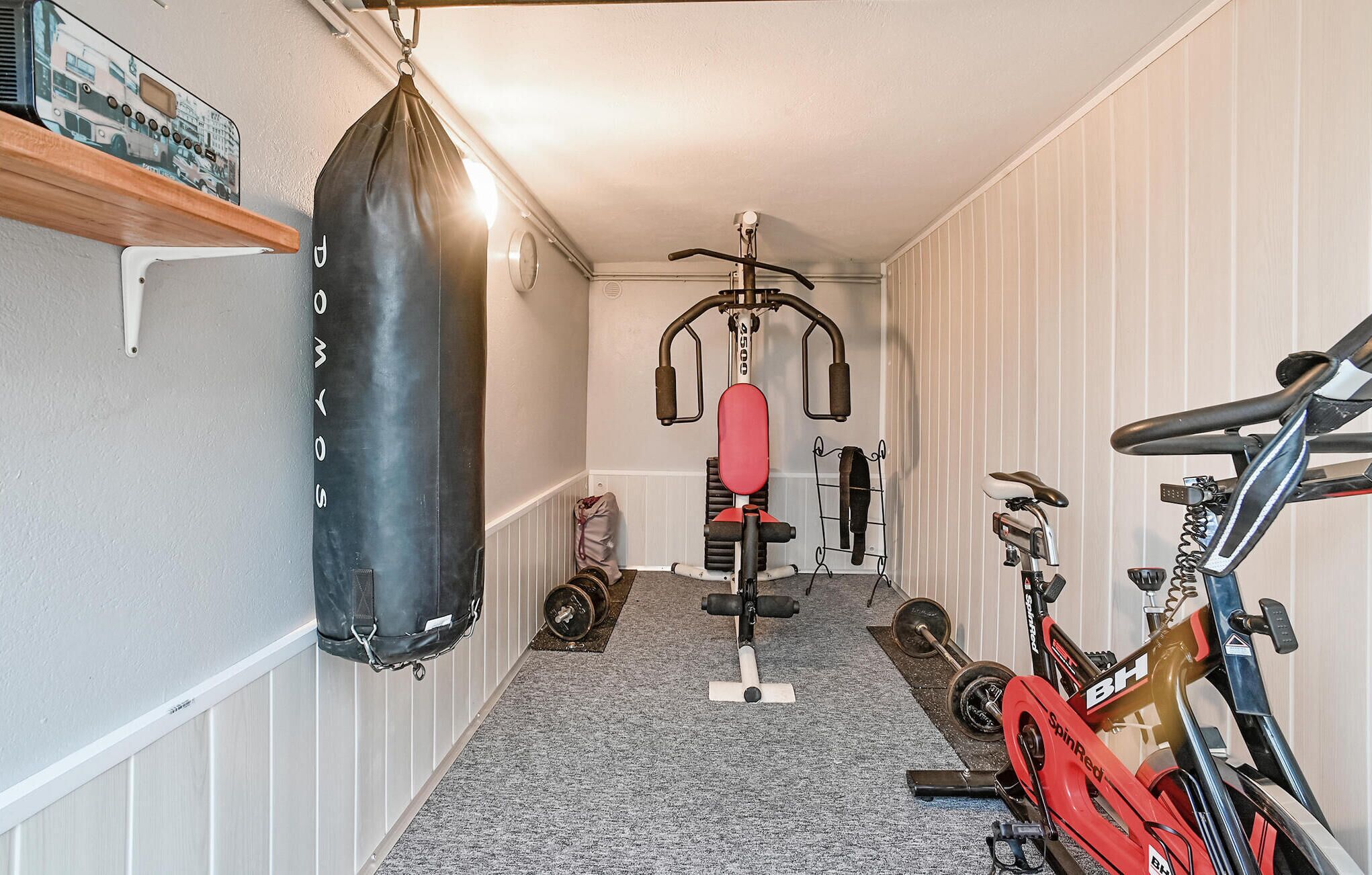 Une salle de sport à domicile équipée d’un sac de frappe, d’un banc de musculation et d’un vélo d’exercice.