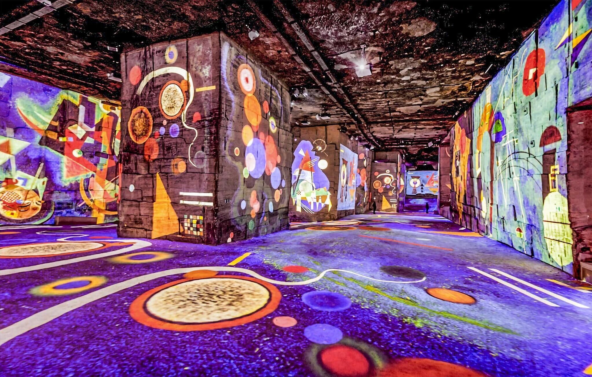 A corridor with colorful graffiti on the walls and floor, featuring abstract shapes and patterns.