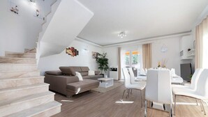 A modern living room with a staircase, a sofa, a dining area, and a kitchen.