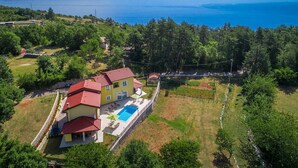 A yellow house with a red roof, a swimming pool, and a view of the sea.