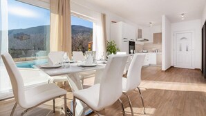 A modern dining area with a pool view, white furniture, and a kitchen in the background.