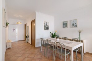A dining area with a white table, grey chairs, and a hanging pendant light.