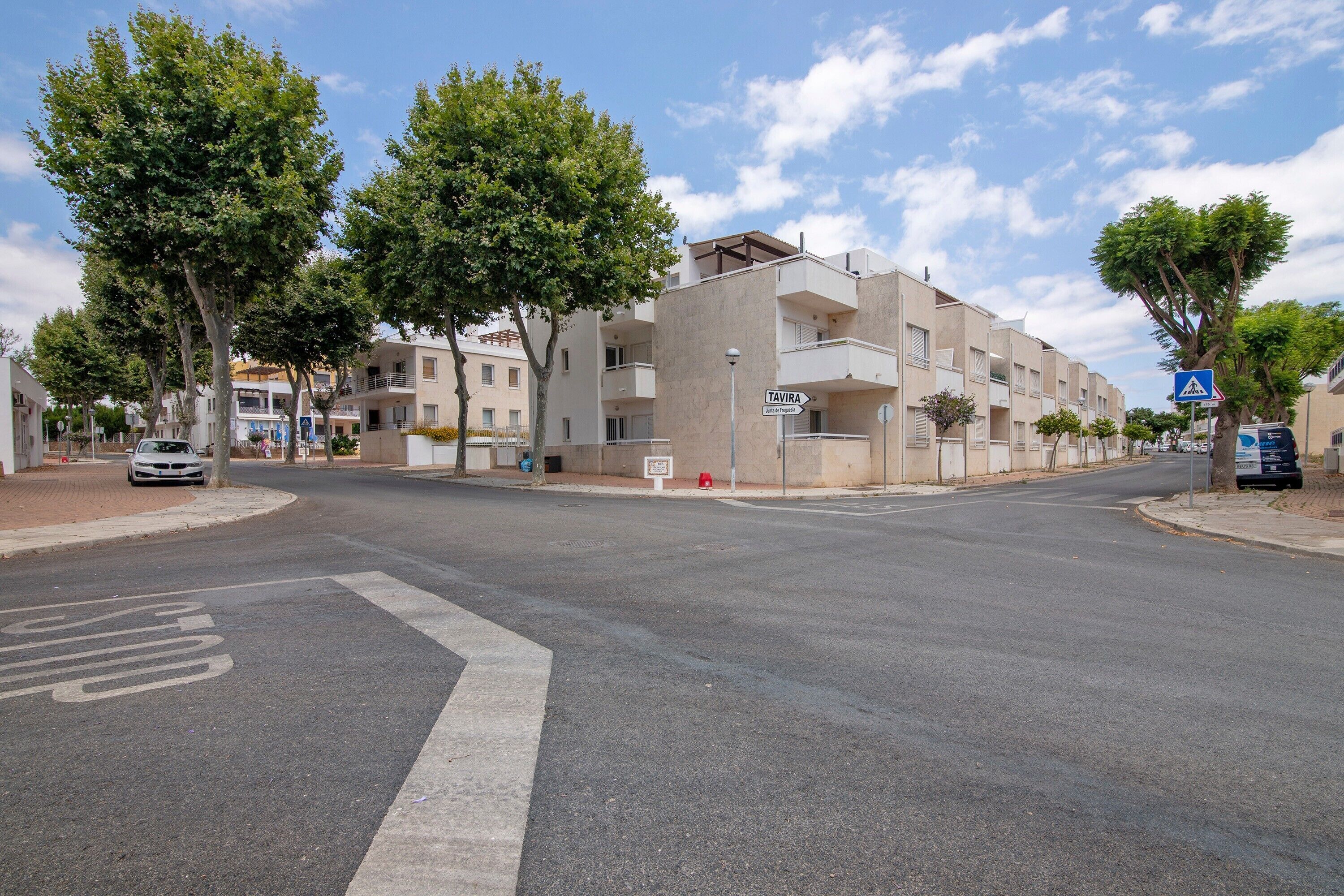 Straatbeeld met een meerlaags gebouw, een zebrapad en een bord met de tekst Tavira.
