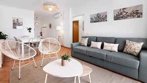 Un salon moderne avec un canapé gris, des chaises blanches, une table ronde et des œuvres d’art murales.