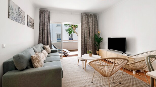 Un salon moderne avec un canapé, des fauteuils, un tél éviseur et un balcon offrant une vue agréable.