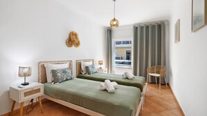 Une chambre avec deux lits, une table de chevet, une lampe, une chaise et une fenêtre avec des rideaux.