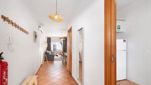 Un couloir avec un extincteur, un banc en bois, un luminaire suspendu et une porte portant un panneau indiquant la sortie de secours.
