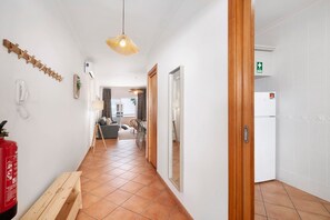 Un couloir avec un extincteur, un banc en bois, un luminaire suspendu et une porte portant un panneau indiquant la sortie de secours.