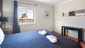 A hotel room with a bed, a desk, a window with a view, and a framed picture on the wall. - Holiday Apartment "Estrela Do Mar" with Wi-Fi (Santa Luzia)