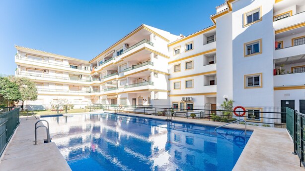 A swimming pool with a clear blue water surface, surrounded by a multi-story building with balconies and a white facade. - Apartment '234 Parque Playa La Cala' with Shared Pool, Wi-Fi and Air Conditioning (la cala de mijas)