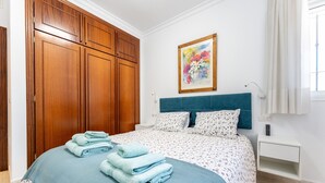 A bedroom with a bed, a nightstand, a wall-mounted painting, and a wooden wardrobe. - Apartment '234 Parque Playa La Cala' with Shared Pool, Wi-Fi and Air Conditioning (la cala de mijas)