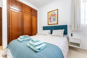 A bedroom with a bed, a nightstand, a wall-mounted painting, and a wooden wardrobe. - Apartment '234 Parque Playa La Cala' with Shared Pool, Wi-Fi and Air Conditioning (la cala de mijas)