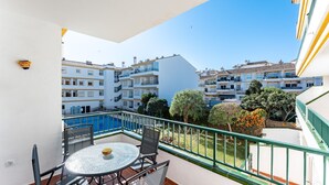 A balcony with a glass table and chairs, overlooking a courtyard with buildings and trees. - Apartment '234 Parque Playa La Cala' with Shared Pool, Wi-Fi and Air Conditioning (la cala de mijas)