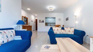 A modern living room with two blue sofas, a wooden coffee table, and a kitchen in the background. - Apartment '234 Parque Playa La Cala' with Shared Pool, Wi-Fi and Air Conditioning (la cala de mijas)