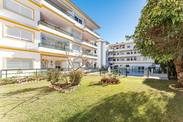 Un hotel de varios pisos con balcones, piscina y un jardín bien cuidado.